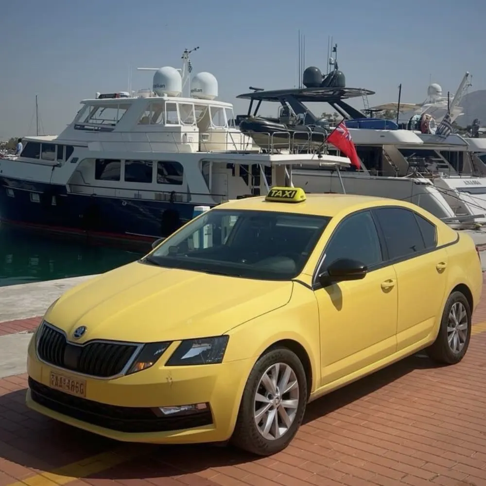 Yellow Skoda taxi parked at a marina in front of yachts